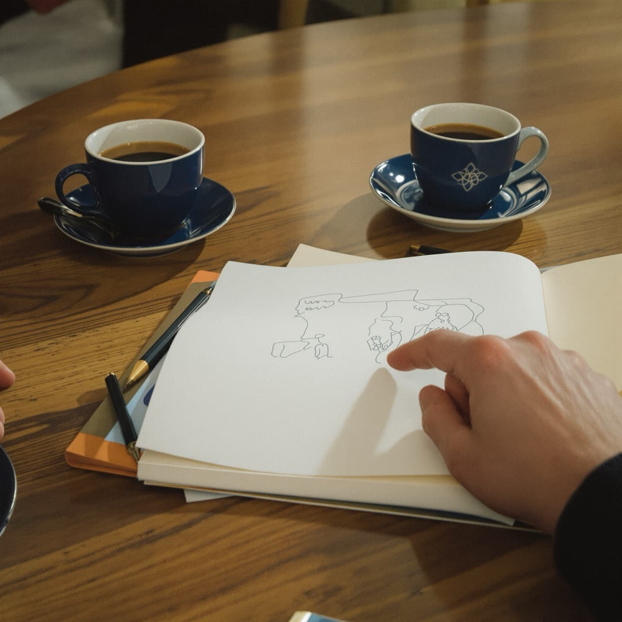 Illustrative image of hands around a table with coffee and a sketch